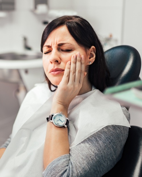 Woman in dental chair holding cheek in pain before emergency dental care