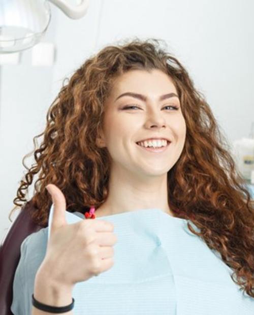 young woman giving thumbs up in dental chair 