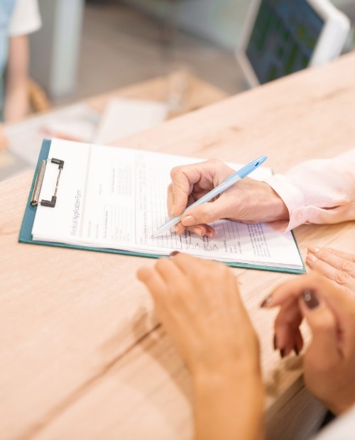 Patient completing dental insurance forms on clipboard