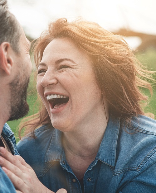 Woman with dental implants in Billerica smiling outside with husband