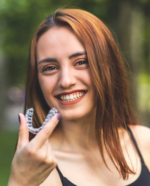 Woman with red hair holding aligner for Invisalign in Billerica, MA