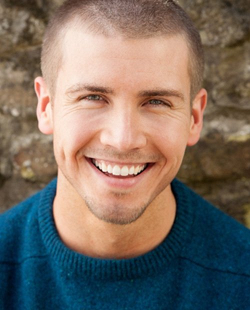 Man in blue shirt standing against wall and smiling