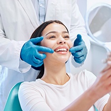 Dentist pointing to patient’s smile that she’s admiring in handheld mirror