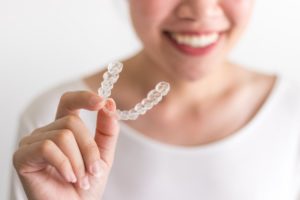 smiling person holding an Invisalign clear aligner 