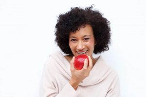 woman with a dental implant chewing a red apple 