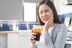 Young woman drinking soda and holding her jaw in pain.