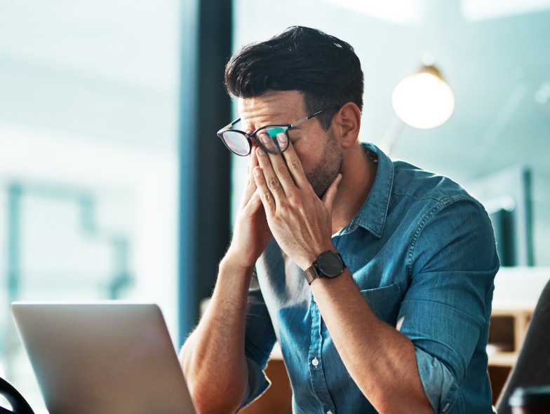 Man in front of laptop rubbing eyes, looking stressed